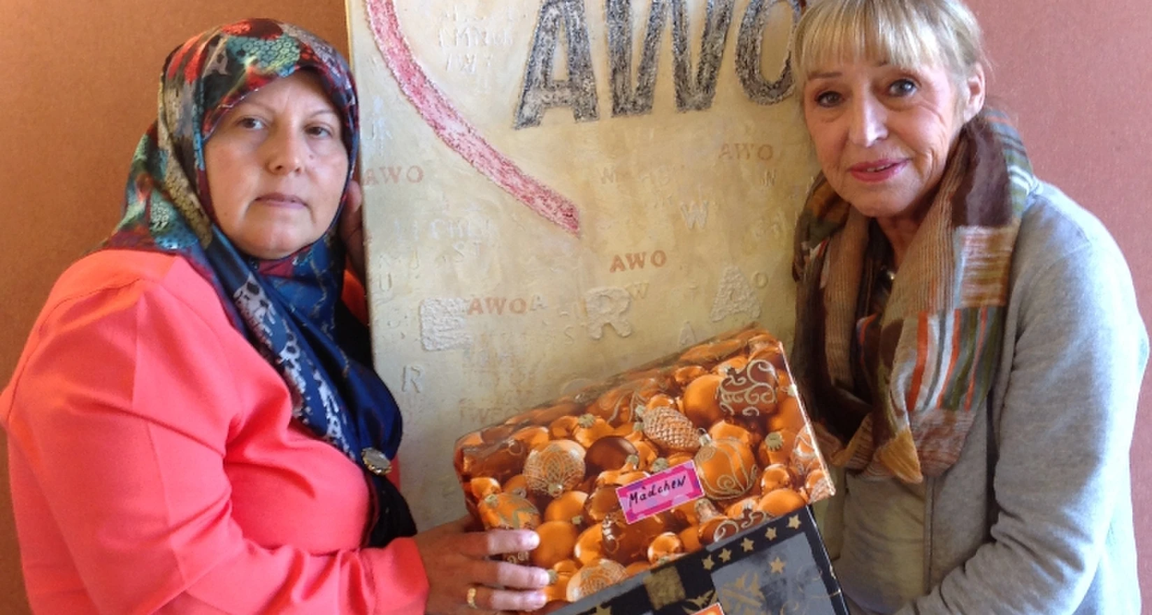 Zwei frauen präsentieren Weihnachtspäckchen vor einem Bild mit dem AWO-Logo